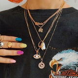 A person wearing multiple gold necklaces with various pendants, including a Zodiac Necklace - Aries, colourful nail polish, and a black shirt with an eagle design.