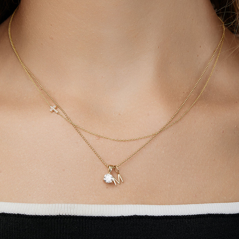 Gold necklace with a small gold letter pendant on a person wearing a black and white top.