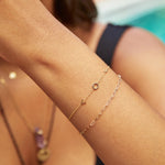 A wrist wearing an Element Short Link Bracelet and a Custom Gold Bracelet with 3 letters (J, O and Y), with a blurred background.