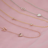 Three necklaces laid on a pink fabric background: a Monogram Necklace with Heart Rose Gold and a letter W charm, a Pavé Monogram Necklace with Diamond and a letter T charm and a Monogram Necklace with Heart White Gold and a letter S charm.