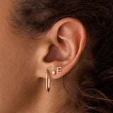 Close-up of a yellow gold Oval Hoop and Monogram Earring Set in a woman’s ear with brown curly hair visible.