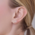 Close-up of a woman's ear wearing Pavé Charm Stud - Hamsa in yellow gold and Pavé Charm Stud - Star of David in white gold, with her blonde hair visible. 