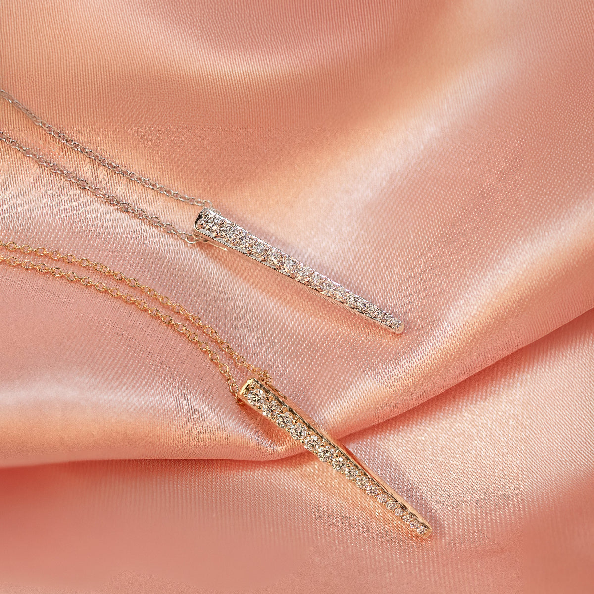 Two Love Struck Diamond Necklaces (one in yellow gold and the other in white gold) on a light orange silk background. 