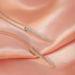 Two Love Struck Diamond Necklaces (one in yellow gold and the other in white gold) on a light orange silk background. 