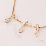 Gold Petite Letter Charms in a b and c on a necklace against a white marble background. 