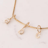 Gold Petite Letter Charms in a b and c on a necklace against a white marble background. 