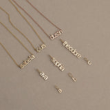 Three Petite Name Plate Necklaces with the names Isabella, Louis and Dustin, three Petite Nameplate Pendants in the names Ava, Sophia and Theodore, and three Petite Letter Charms in lowercase a, b and c, all in yellow gold, against a beige background. 