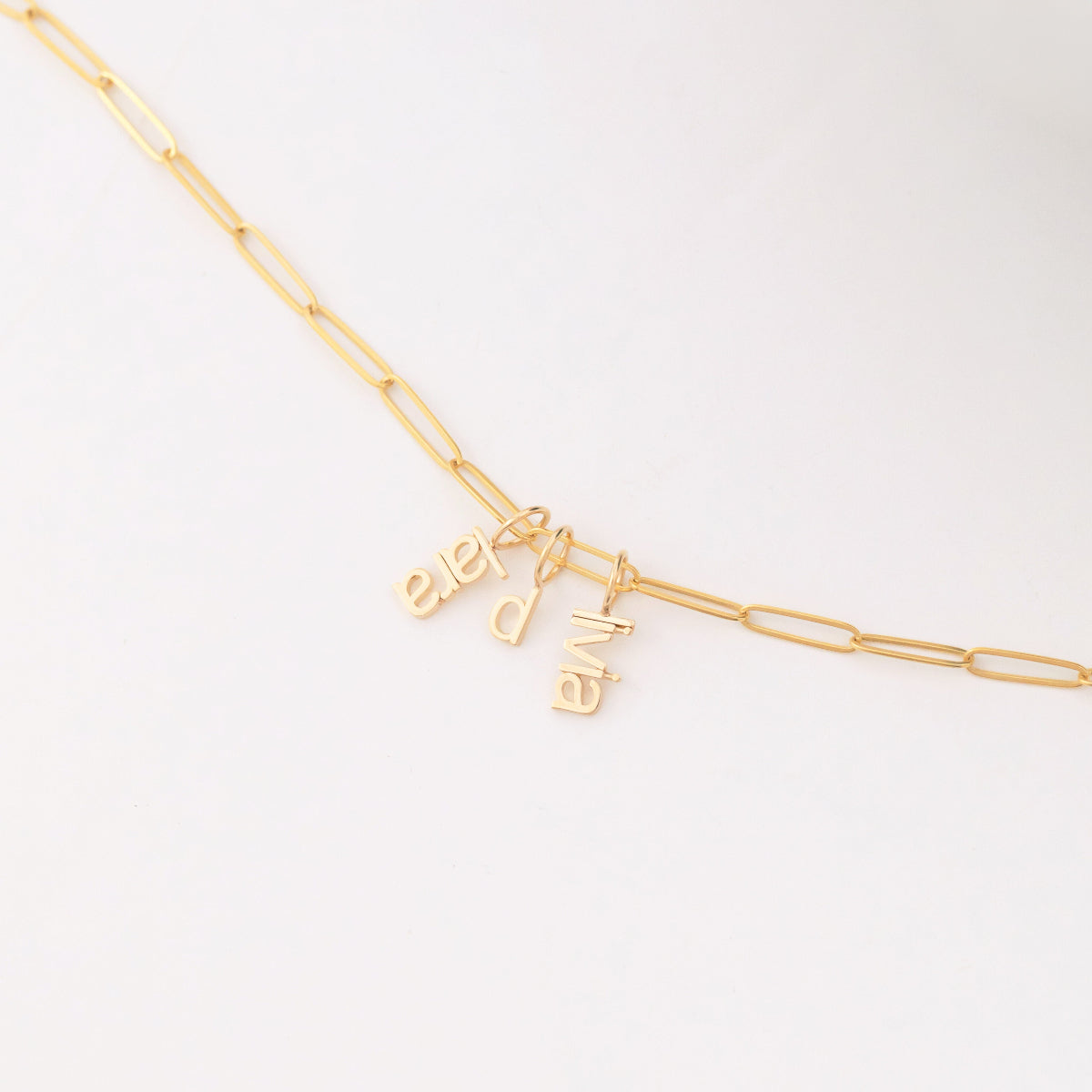 An Element Long Link Chain with three Petite Nameplate Pendants, 'lara', 'd' and 'livia', all in yellow gold on a white background. 