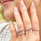 Close-up of a woman's hand wearing multiple stacked rings, including two Bouquet Rings, a Birthstone Ring, a C Letter Ring and Delicate Beaded Bands. 