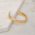 A vermeil gold All in Cuff on a light marble surface.