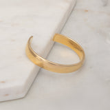 A vermeil gold All in Cuff on a light marble surface.