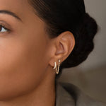 Close-up of woman's ear wearing a White Topaz Chain Earring and a Pave Huggie against a blurred background. 
