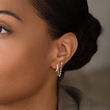 Close-up of woman's ear wearing a White Topaz Chain Earring and a Pave Huggie against a blurred background. 