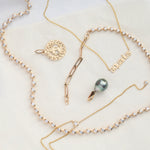 The Ultimate Diamond Necklace, a Petite Zodiac Necklace 'aquarius', a Diamond Drip Necklace, a Zodiac Pendant and a Baroque Pearl Pendant laid on a cream background. 