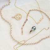 The Ultimate Diamond Necklace, a Petite Zodiac Necklace 'aquarius', a Diamond Drip Necklace, a Zodiac Pendant and a Baroque Pearl Pendant laid on a cream background. 