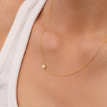 Gold necklace with a small gold four leaf clover charm on a person wearing a white top.