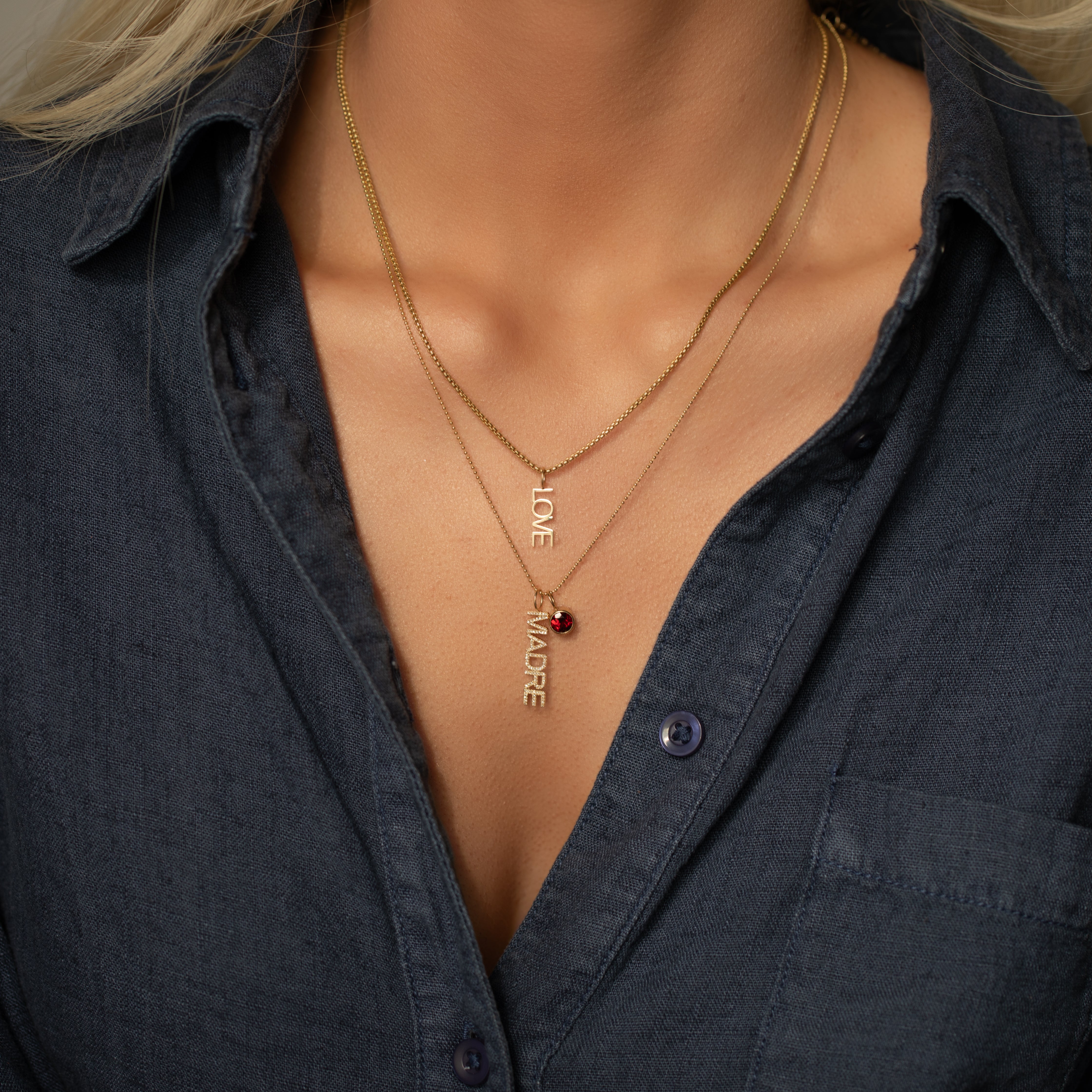 Close-up of a person wearing layered gold necklaces with visible text and a red gemstone.