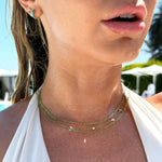 Close-up of a woman's neck wearing two Confetti Necklaces - Green, a Custom Gold Necklace - 5 Letters, an Alli Webb Turquoise Huggie and a Pavé Charm Stud - Moon, styled in a white halter top with blonde wet hair.