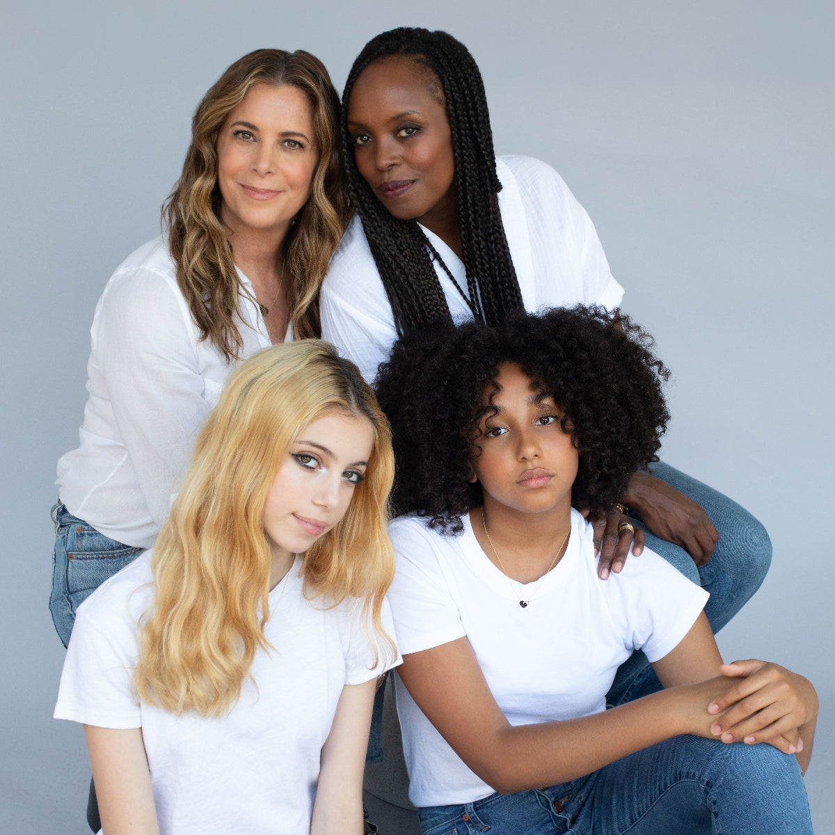 Two women and their daughters all wearing the Enamel Gold Unity Pendant, styled with white tops and blue jeans against a light grey background.