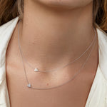 A close-up of a woman's neck wearing two white gold 14k Gold Asymmetrical Charm Necklaces in - Heart and Pavé Heart, styled in a white jacket.