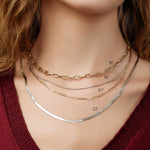 Close-up of a neck wearing a yellow gold Bold Link Chain, a white gold Box Chain, a yellow gold Element Long Link Chain and a white gold Sequence Chain, with orange hair and styled with a deep red top. 