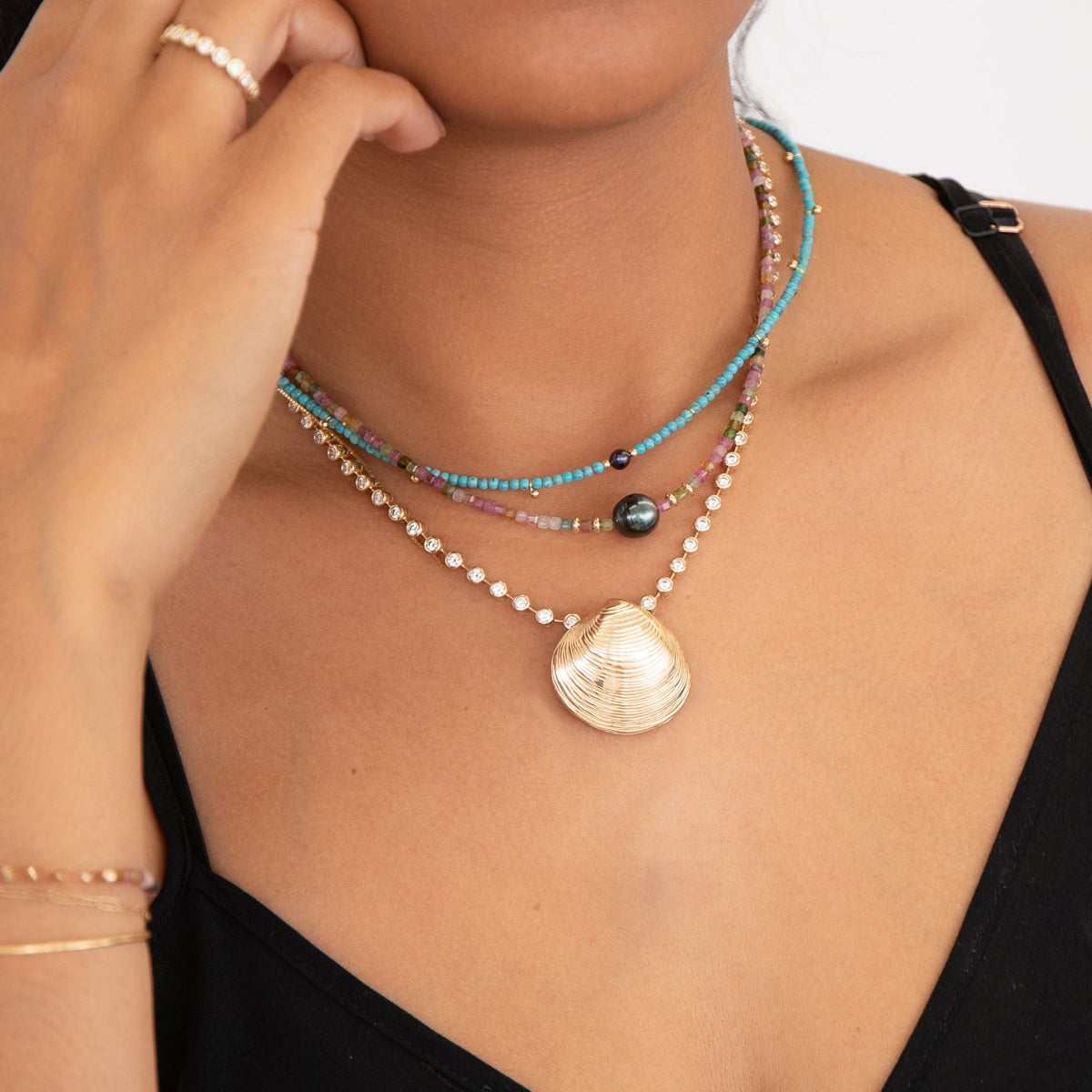 Close-up of a woman's neck wearing Endless Summer Necklaces in Sweet Escape and Santorini, The Ultimate Diamond Necklace with The Golden Venus Shell and The Evermore Ring, styled in a black strap top. 
