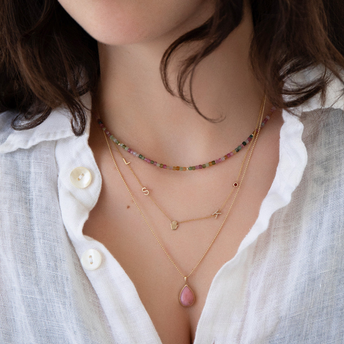 Close-up of a woman's neck wearing an Endless Summer Necklace - Coral Reef, Custom Gold Necklace - 5 Letters, a Classic Bead Chain with a Pink Opal Tear Drop Charm, styled in a white shirt. 