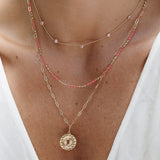 Close-up of a neck wearing a Quintet Birthstone Layering Necklace, a Confetti Necklace - Pink and a Zodiac Necklace - Pisces, styled in a white top. 