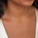 Close-up of a neck wearing a yellow gold Triple Diamond Layering Necklace and a 14k Gold Asymmetrical Letter Necklace - H in yellow gold with a white top. 