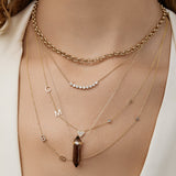 A close-up of a woman's décolletage wearing a Rolo Necklace, a Diamond Arc Layering Necklace, Custom Gold Necklaces - 5 Letters and 3 Letters, and The Courage Retreat Necklace, styled in a white top. 