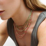 Close-up of a woman wearing several Confetti Necklaces in Green, Yellow, Pink and Blue, styled in a grey top. 