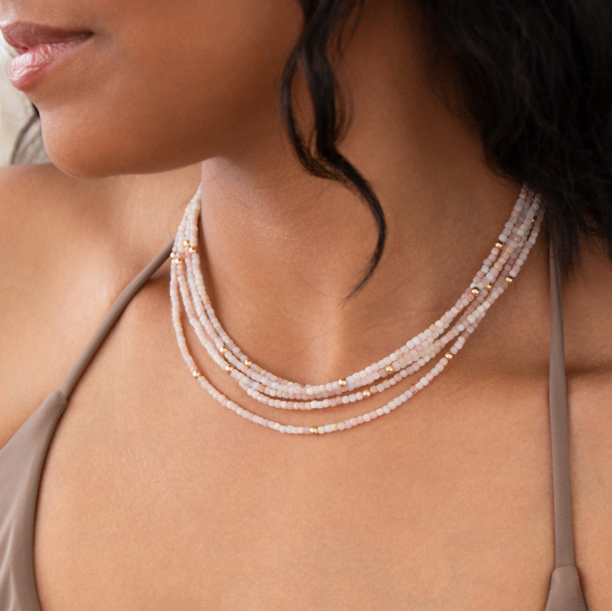 Close-up of a woman's neck wearing several Endless Summer Necklaces in Pink Sands, styled with a taupe strap top. 