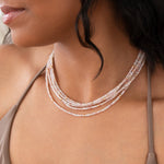 Close-up of a woman's neck wearing several Endless Summer Necklaces in Pink Sands, styled with a taupe strap top. 