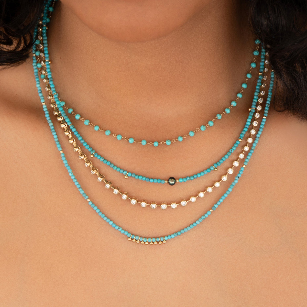 Close-up of a neck wearing The Bluebell Bouquet Necklace, Endless Summer Necklaces in Turqs + Caicos and Santorini, and The Ultimate Diamond Necklace.