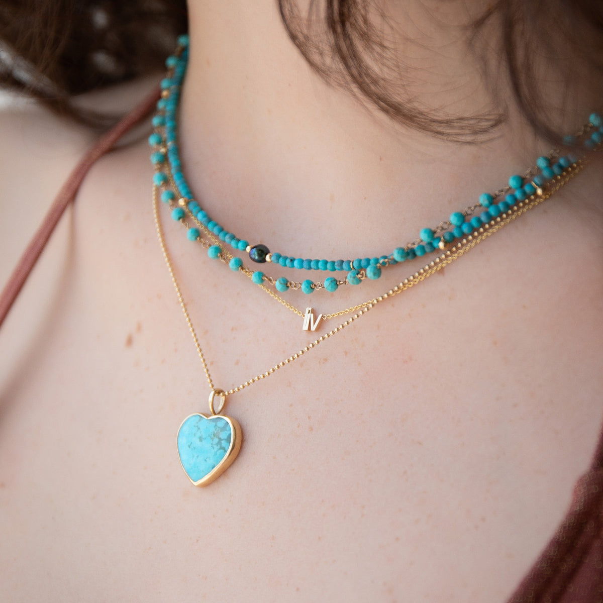 Close-up of a person wearing multiple necklaces with turquoise beads and a heart-shaped pendant.