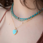 Close-up of a person wearing multiple necklaces with turquoise beads and a heart-shaped pendant.
