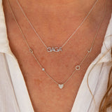 A close-up of a décolletage wearing a GAGA Necklace and a Custom Gold Necklace - 5 Letters, both in white gold and white shirt. 