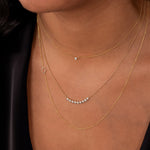 Close-up of a neck wearing a Single Diamond Layering Necklace, a Diamond Arc Layering Necklace and a 14k Gold Asymmetrical Letter Necklace - O all in yellow gold, with a black silk top.