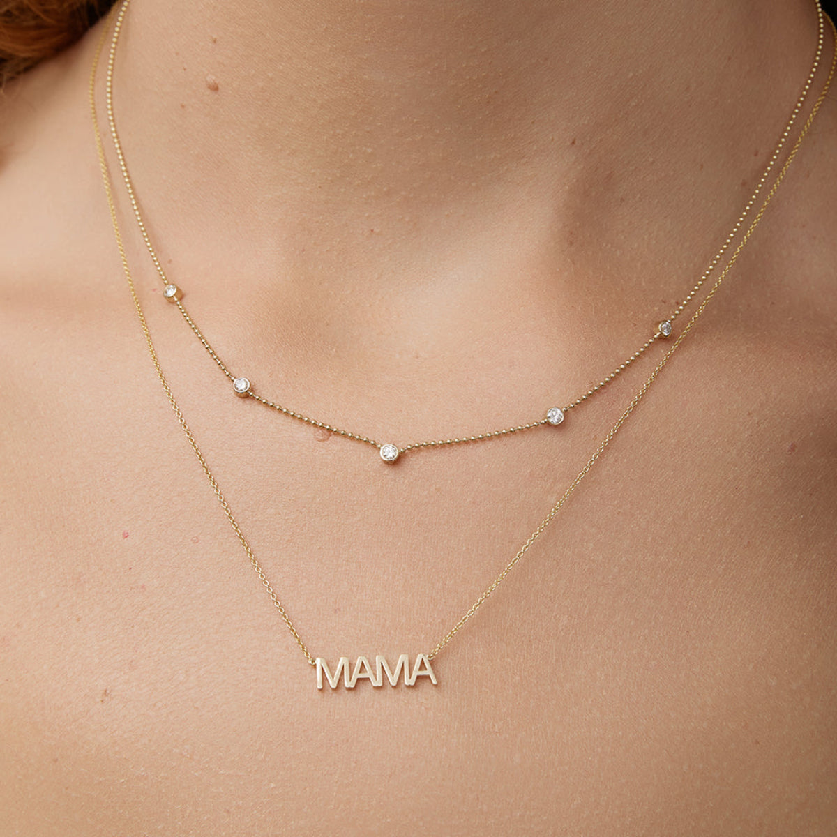 Close-up of a neck wearing Quintet Diamond Layering Necklace and a MAMA Necklace in yellow gold. 