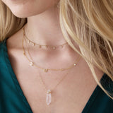 Close-up of a blonde woman's neck wearing a Stardust Diamond Necklace, a Custom Gold Necklace - 5 Letters and The Clarity Retreat Necklace, styled with an emerald green top. 