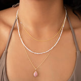 Close-up of a woman's neck wearing a 14k Gold Asymmetrical Letter Necklace - A in yellow gold, an Endless Summer Necklace - Pink Sands, a Classic Bead Chain with a Pink Opal Tear Drop Charm.  
