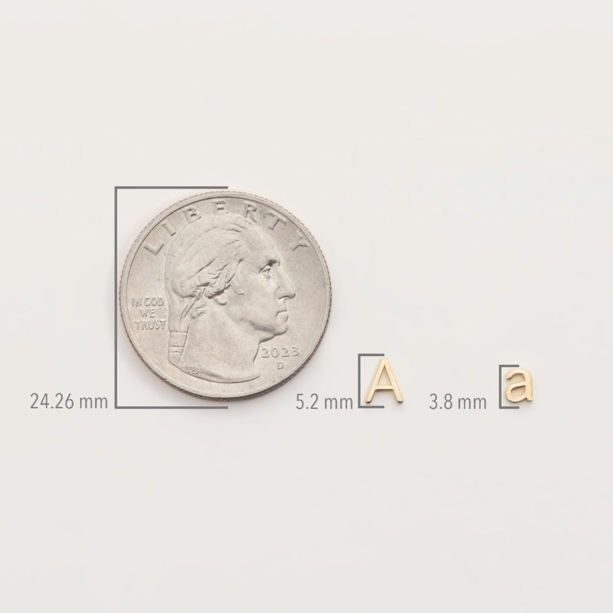 A silver coin with measurements shown with a Petite Letter Charm a and a Gold Letter Charm A on a white background. 