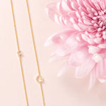 Two yellow gold necklaces with single letter charms, F and G, displayed on a neutral background with a pink flower.