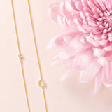 Two yellow gold necklaces with single letter charms, F and G, displayed on a neutral background with a pink flower.