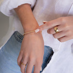 A close-up of a hand wearing a Little Bubble Bracelet, two Delicate Beaded Bands, a Twinkle Twinkle Ring and a Thick Band, with a white shirt and blue jeans. 