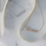 A Pavé Madre Necklace in white gold and a Pavé MOMMY Necklace in yellow gold on a white marble background. 