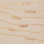 MAMA, Pavé MADRE, Pavé GAGA, Pavé MIMI, GIGI and Pavé NANA Necklaces in yellow or rose gold laid against a light beige background. 