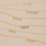 MAMA, Pavé MADRE, Pavé GAGA, Pavé MIMI, GIGI and Pavé NANA Necklaces in yellow or rose gold laid against a light beige background. 
