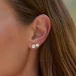 Close-up of an ear wearing two diamond stud earrings with blurred background