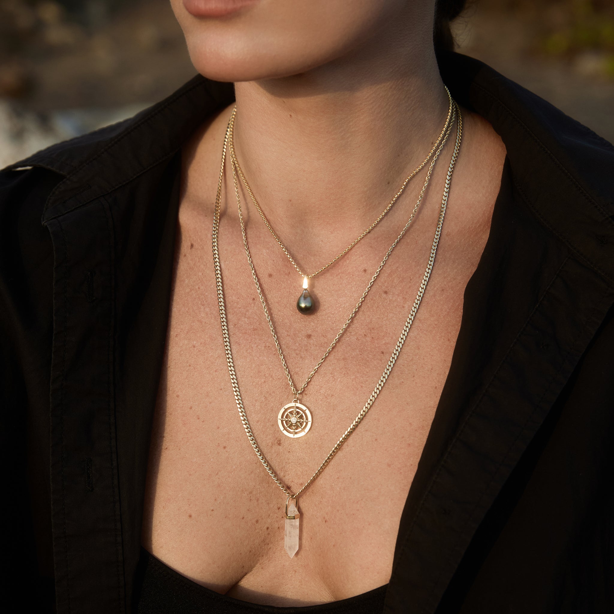 Model wearing the Baroque Pearl Pendant on a gold chain layered with gold charm necklaces.